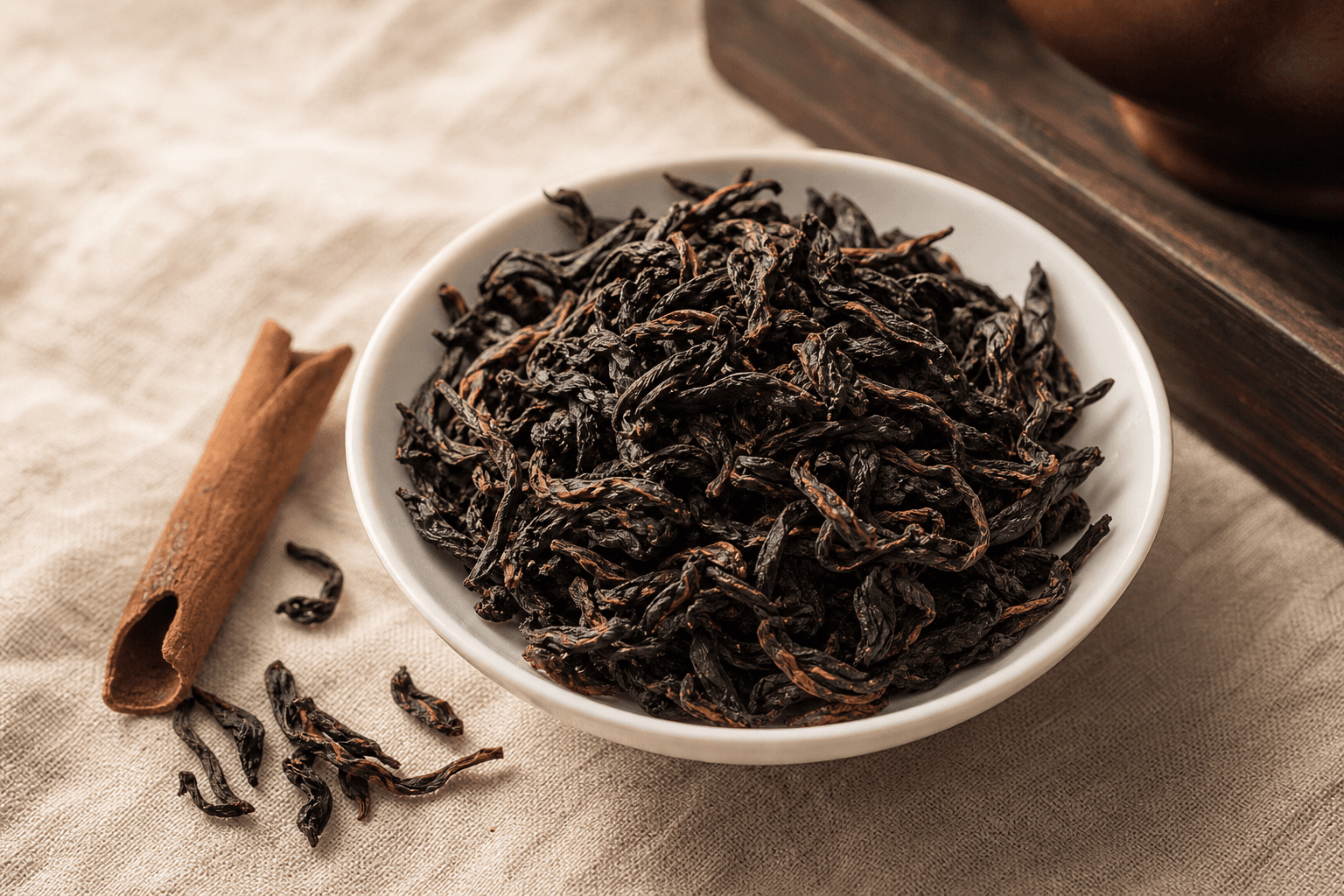 Close-up of long dark twisted Rou Gui leaves on cream linen with a small piece of cassia bark resting alongside