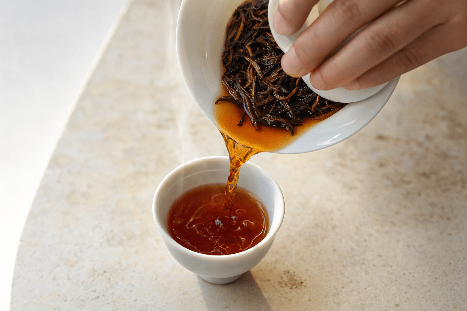 Clear reddish-brown Yunnan Crown Reserve Black Tea poured from a white gaiwan into a small cup, steam rising